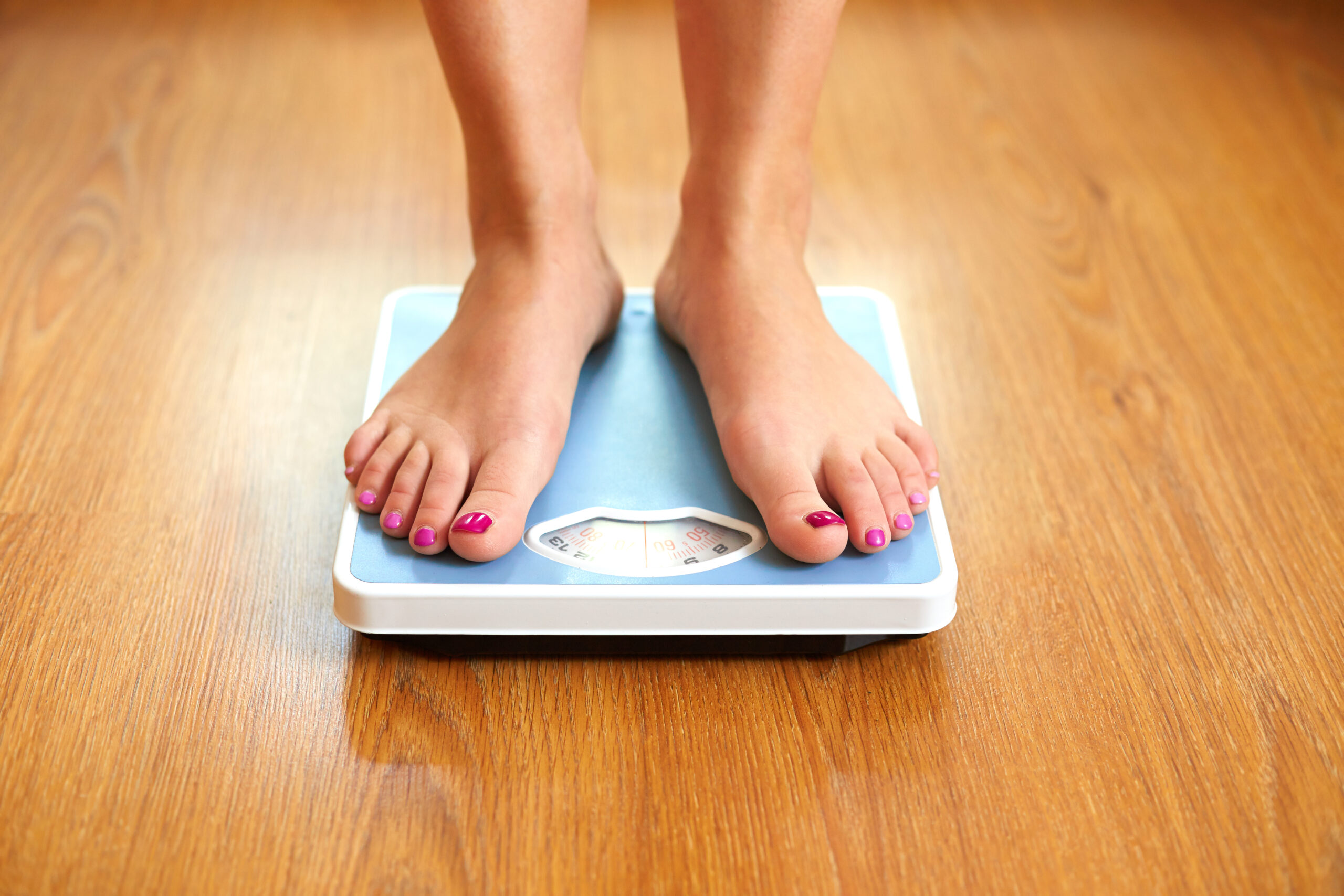 Woman standing on blue weight scale to measure her weight loss goals.